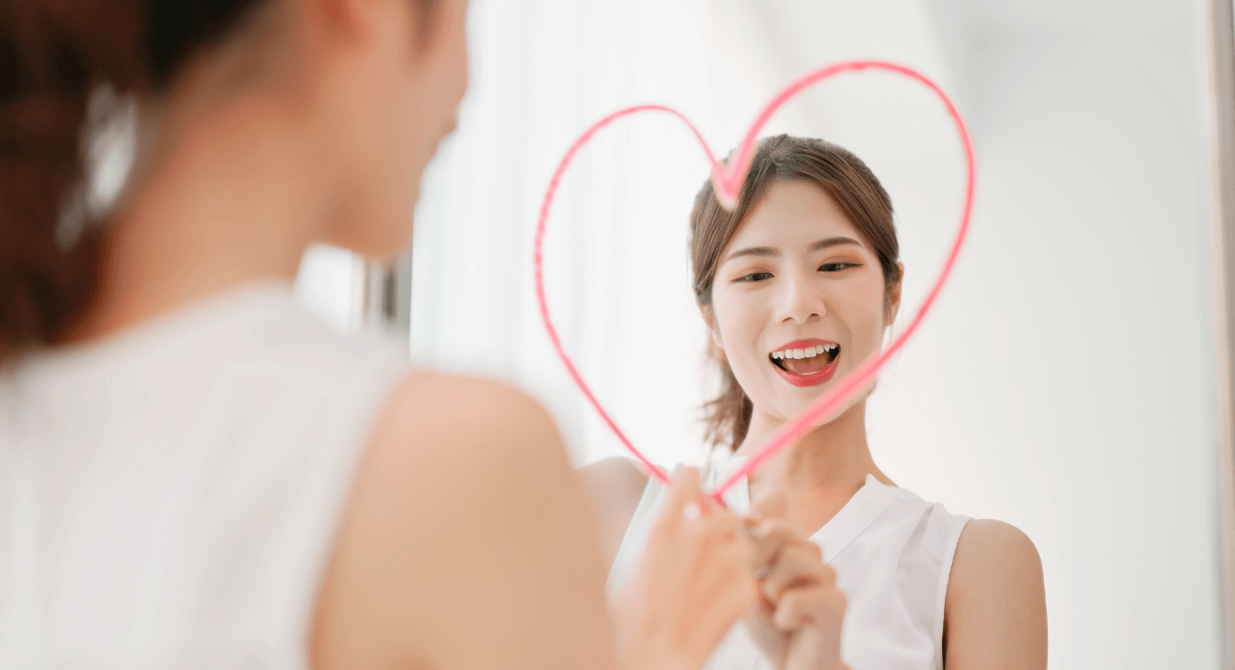 Mujer mirándose al espejo con un corazón dibujado con labial, simbolizando la recuperación de su autoestima y el amor propio después de una herida emocional
